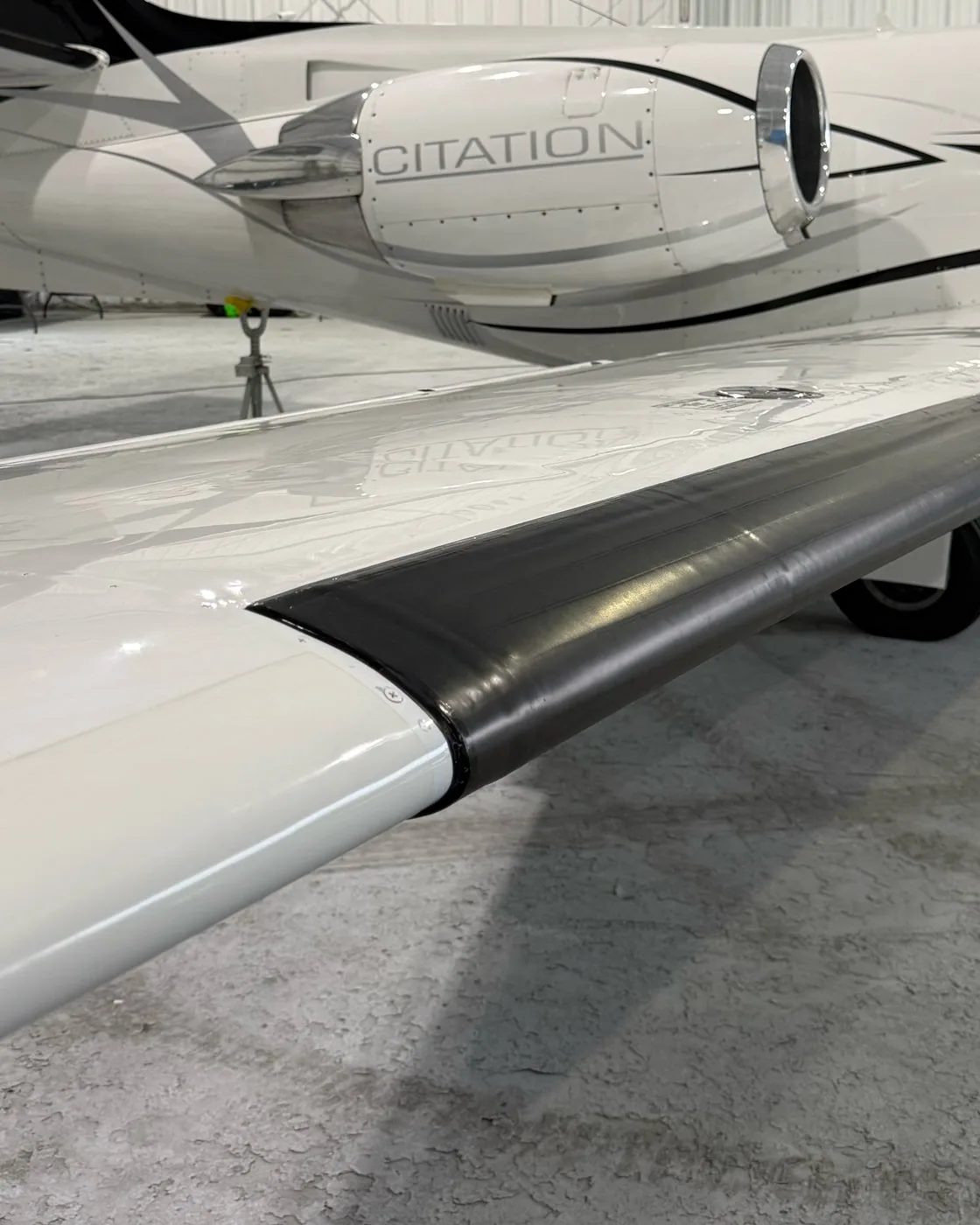 The wing of a Citation business jet in a hangar, the structure overhead mirrored in its finish